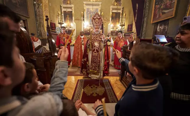 Children hold candles as Iraq-born Armenian church Archbishop Datev Hagopian prepares to share the holy light during the Orthodox Easter service at the Armenian cathedral in Bucharest, Romania, Saturday, April 19, 2025. (AP Photo/Andreea Alexandru)