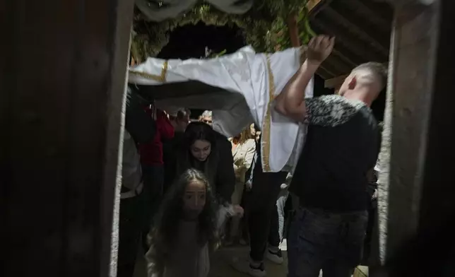 Greek Orthodox Christian worshipers pass under the Epitaphios depicting Jesus Christ's preparation for burial, during the Good Friday procession at Agios Epifanios church in Droushia village in Paphos district on holy Friday, April 18, 2025. (AP Photo/Petros Karadjias)