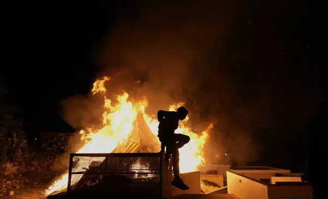 A young man is seen in front of the traditional Easter bonfire, or lambratzia, where effigies of Judas Iscariot, the disciple believed to have betrayed Jesus, are burned during Easter celebrations at the church of Agios Epifanios in the village of Droushia in the Paphos district on the Akamas peninsula on holy Saturday, April 19, 2025, in Cyprus. (AP Photo/Petros Karadjias),