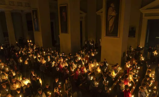 Worshippers hold candles during the Easter vigil Mass in the Cathedral Basilica of Vilnius, Lithuania, late Saturday, April 19, 2025. (AP Photo/Mindaugas Kulbis)