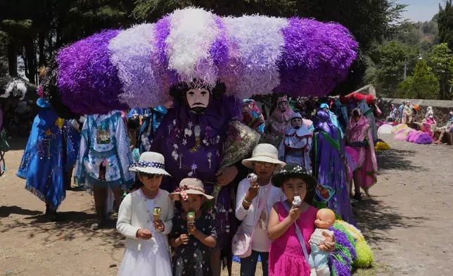 Children pose for a photo with a reveler, known as a sayon, in a tissue paper hat during Easter Day celebrations in Tetela del Volcan, Mexico, Sunday, April 20, 2025. (AP Photo/Eduardo Verdugo)