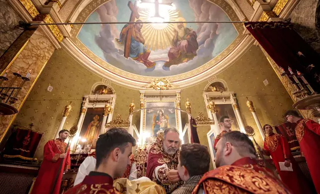 A boy receives the holy communion from Iraq-born Armenian church Archbishop Datev Hagopian during the Orthodox Easter service at the Armenian cathedral in Bucharest, Romania, Saturday, April 19, 2025. (AP Photo/Andreea Alexandru)