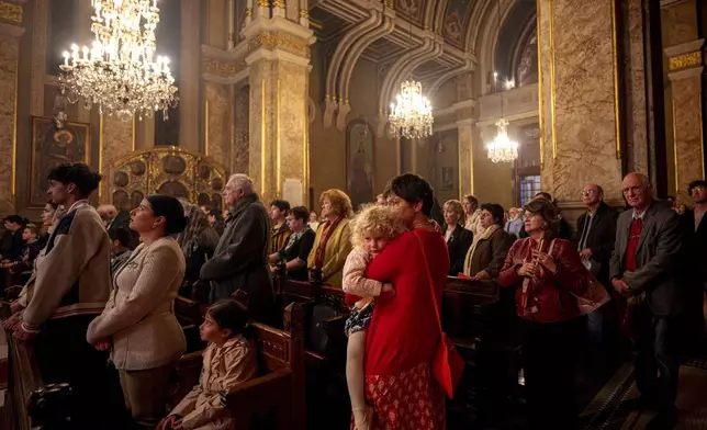 A woman holds a child during the Orthodox Easter service at the Armenian cathedral in Bucharest, Romania, Saturday, April 19, 2025. (AP Photo/Andreea Alexandru)