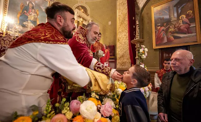 A boy receives the holy communion from Iraq-born Armenian church Archbishop Datev Hagopian during the Orthodox Easter service at the Armenian cathedral in Bucharest, Romania, Saturday, April 19, 2025. (AP Photo/Andreea Alexandru)