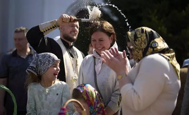 Believers are blessed by Russian Orthodox priest Father Anastasius, as people carry their baskets containing traditional cakes and painted eggs to be blessed in preparation for an Easter celebration at the St. Boris and Gleb Monastery in the old Russian town of Dmitrov, some 70 km (44 miles) north of Moscow, Russia, Saturday, April 19, 2025. (AP Photo/Alexander Zemlianichenko)