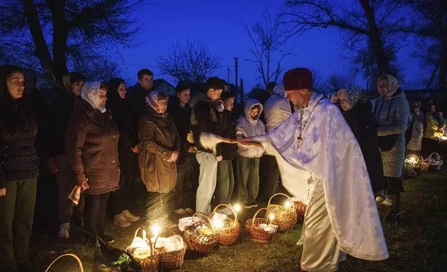 Priest Serhii Zezul blesses Easter baskets in front of a church destroyed in fighting between Russian and Ukrainian forces, during celebration of the Orthodox Easter in Lukashivka village, Ukraine, on Sunday, April 20, 2025. (AP Photo/Evgeniy Maloletka)