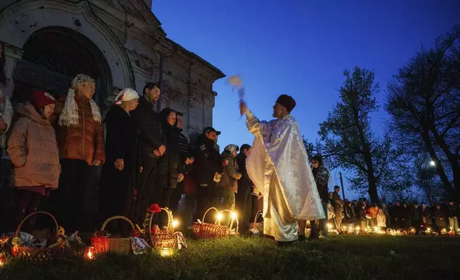 Priest Serhii Zezul blesses Easter baskets in front of a church destroyed in fighting between Russian and Ukrainian forces, during celebration of the Orthodox Easter in Lukashivka village, Ukraine, on Sunday, April 20, 2025. (AP Photo/Evgeniy Maloletka)
