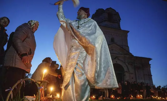 A priest Serhii Zezul blesses Easter baskets in front of a church destroyed in fighting between Russian and Ukrainian forces, during celebration of the Orthodox Easter in Lukashivka village, Ukraine, on Sunday, April 20, 2025. (AP Photo/Evgeniy Maloletka)