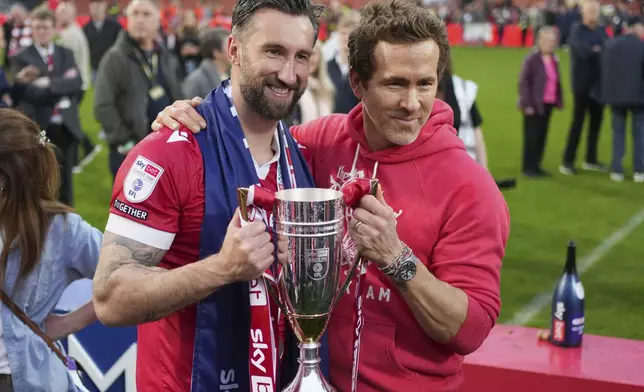 Wrexham co-owner Ryan Reynolds, right, and Wrexham's Ollie Palmer pose with trophy at the end of the English League One soccer match between Wrexham and Charlton Athletic at the Racecourse ground in Wrexham, Wales, Saturday, April 26, 2025. (AP Photo/Jon Super)
