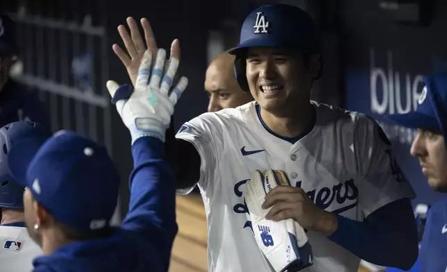 Los Angeles Dodgers' Shohei Ohtani celebrates in the dugout after scoring on a three-run home run by Will Smith during the third inning of a baseball game in Los Angeles, Tuesday, April 15, 2025. (AP Photo/Kyusung Gong)