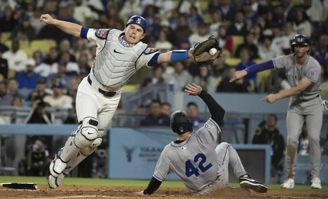 Colorado Rockies' Mickey Moniak, bottom, scores past Los Angeles Dodgers catcher Will Smith during the fourth inning of a baseball game in Los Angeles, Tuesday, April 15, 2025. (AP Photo/Kyusung Gong)