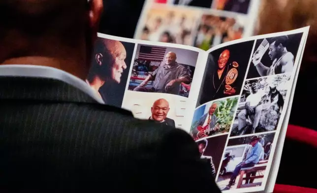 A mourner looks through photos in a program during a memorial service for Olympic and world champion boxer and minister George Foreman at Wortham Theater Center in Houston, Monday, April 14, 2025. (Brett Coomer/Houston Chronicle via AP)