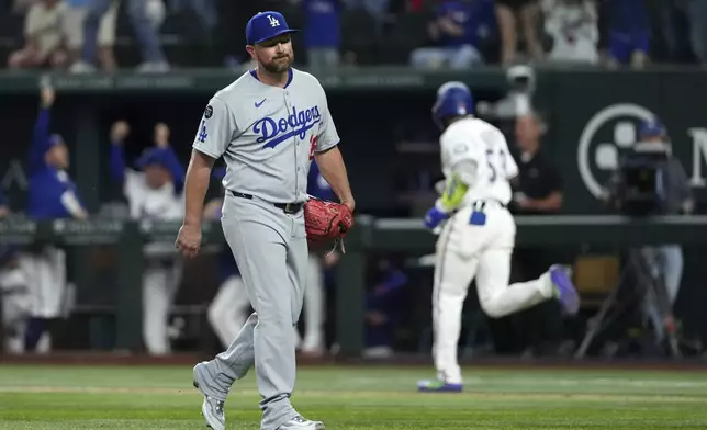 Los Angeles Dodgers pitcher Kirby Yates, foreground, walks off the field after giving up a walkoff two-run home run to Texas Rangers' Adolis García, back right, that also scored Josh Smith during the ninth inning of a baseball game Saturday, April 19, 2025, in Arlington, Texas. (AP Photo/Jeffrey McWhorter)
