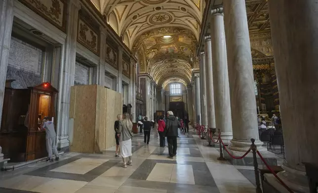 People walk past a wooden board where work in progress is taking place on the spot where Pope Francis will be buried, inside St. Mary Major basilica, in Rome, Tuesday, April 22, 2025. (AP Photo/Alessandra Tarantino)