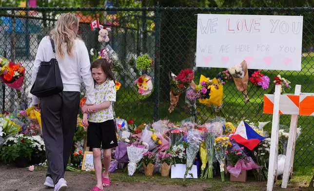 Visitors stand near a growing memorial the day after a driver killed multiple people during a Filipino community festival Sunday, April 27, 2025, in Vancouver, British Columbia. (AP Photo/Lindsey Wasson)