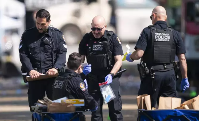 Members of the Vancouver Police forensics team examine a victim's identification while investigating the scene where a vehicle drove into a crowd Saturday at a street festival, in Vancouver, British Columbia, Sunday, April 27, 2025. (Rich Lam/The Canadian Press via AP)