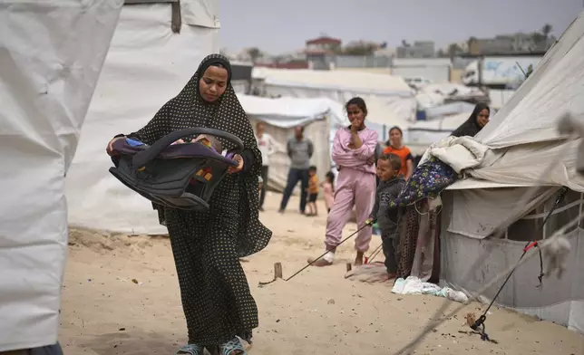 Shaima Al-Louh, 24, carries her 3-month-old daughter, Jilan Zarrouk, at a makeshift tent camp for displaced Palestinians in Muwasi, on the outskirts of Khan Younis in the southern Gaza Strip, on Wednesday, April 9, 2025. (AP Photo/Abdel Kareem Hana)