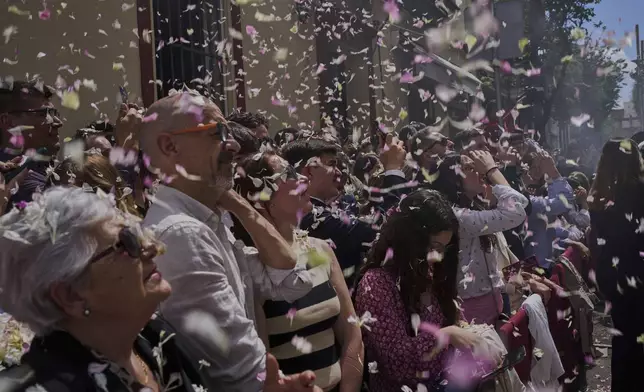 People are showered with flower petals are thrown from balconies during a Holy Week procession in Seville, Spain, Sunday, April 13, 2025. (AP Photo/Emilio Morenatti)