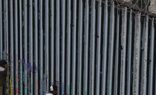 FILE - Young men peer through the border wall as U.S. Border Patrol in San Diego prepare for the arrival of hundreds of pro-migration protesters, in Tijuana, Mexico, Dec. 10, 2018. (AP Photo/Rebecca Blackwell, File)