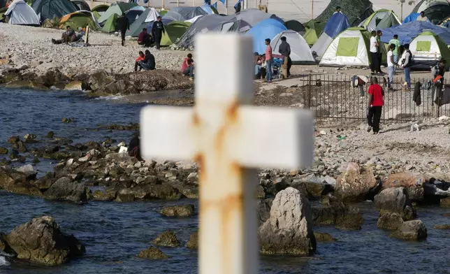 FILE - Migrants and refugees walk behind a cross in a camp set up by volunteers near the port of Mytilini, on the Greek island of Lesbos, April 15, 2016. (AP Photo/Petros Giannakouris, File)