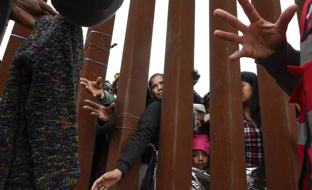 FILE - Migrants reach through a border wall for clothing handed out by volunteers as they wait for asylum, May 12, 2023, in San Diego, Texas. (AP Photo/Gregory Bull, File)