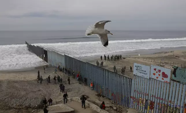 FILE - People peer through the border wall as U.S. Border Patrol in San Diego prepare for the arrival of hundreds of pro-migration protesters, in Tijuana, Mexico, Dec. 10, 2018. (AP Photo/Rebecca Blackwell, File)