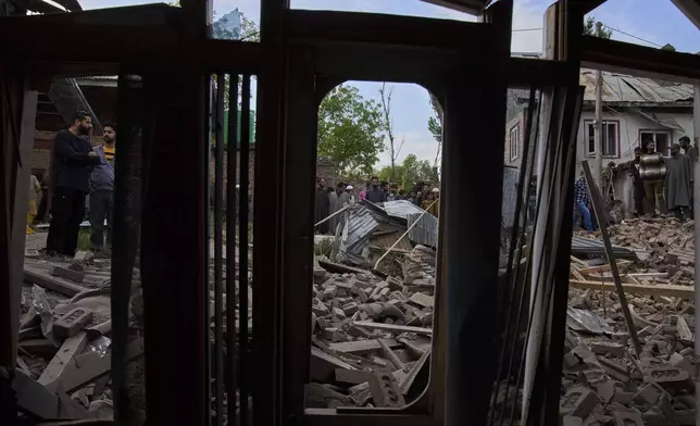 Kashmiri villagers inspect the debris of the blown-up family home of Ahsan Ul Haq Shiekh, a militant who officials say is involved in the deadly attack on tourists in Pahalgam, seen through the window of partially damaged house of a neighbor at Murran village in Pulwama, south of Srinagar, Indian controlled Kashmir, Saturday, April 26, 2025. (AP Photo/Dar Yasin)