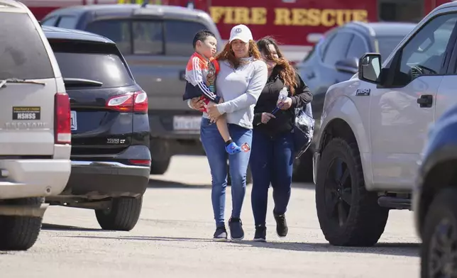 A woman carries a child as she and a student of Wilmer-Hutchins High School leave after authorities reported the campus had been secured following reports of a shooting, in Dallas, Tuesday, April 15, 2025. (AP Photo/Julio Cortez)