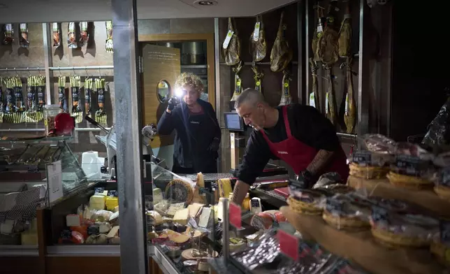 Vendors use their phone light to select and save some food, during a major power outage in Barcelona, Spain, Monday, April 28, 2025. (AP Photo/Emilio Morenatti)