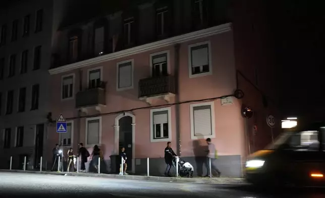 People walk along an unlit street in Lisbon, during a nationwide power outage, Monday night, April 28, 2025. (AP Photo/Armando Franca)