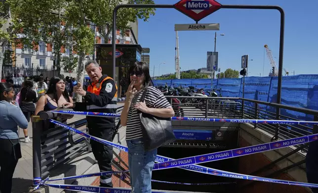 A security guard speaks with a woman outside a temporarily closed metro station during a nationwide power outage in Madrid, Monday, April 28, 2025. (AP Photo/Manu Fernandez)