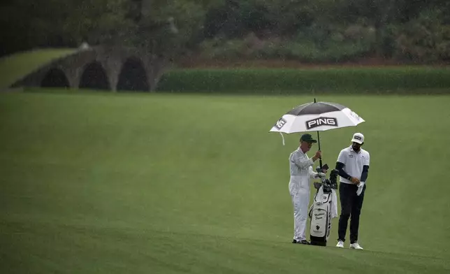 Matthieu Pavon, of France, keeps dry on the 13th fairway with caddie Mark Sherwood, left, during a practice round at the Masters golf tournament, Monday, April 7, 2025, in Augusta, Ga. (AP Photo/Ashley Landis)