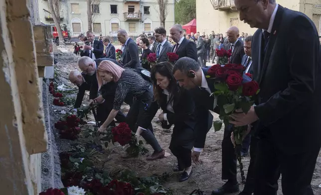 Representatives of embassies place flowers on a wall of a house destroyed by Thursday's Russian strike on a residential neighborhood in Kyiv, Ukraine, on Friday, April 25, 2025. (AP Photo/Evgeniy Maloletka)