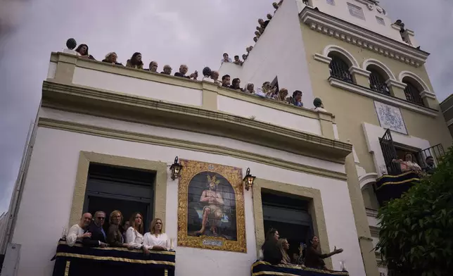 People watch from balconies and rooftops as the statue of the Christ of the brotherhood of La Estrella is carried in procession during the Holy Week in Seville, Spain, Sunday, April 13, 2025. (AP Photo/Emilio Morenatti)