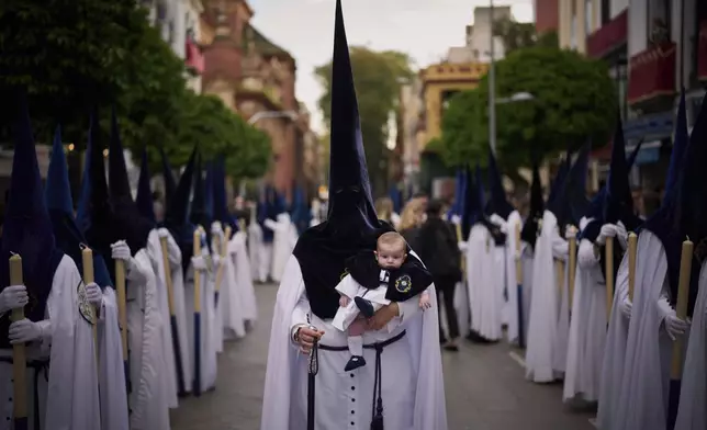 A penitent holds his six-month-old son as he processes through the streets of Seville during Holy Week in Spain, Sunday, April 13, 2025. (AP Photo/Emilio Morenatti)