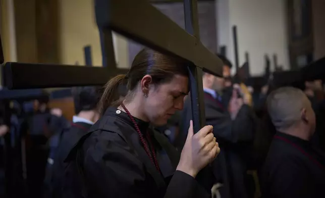 A penitent holds her cross as she prays before the start of the procession in the brotherhood of La Sed, during Holy Week in Seville, Spain, Wednesday 16 April, 2025. (AP Photo/Emilio Morenatti)