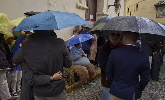 Visitors shelter from the rain with their umbrellas as they wait in vain for the departure of the processions cancelled due to rain, during Holy Week in Seville, Spain, Tuesday, April 15, 2025. (AP Photo/Emilio Morenatti)