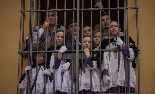 Altar servers crowd a window to watch the passing of the Christ of the San Bernardo brotherhood during Holy Week in Seville, Spain, Wednesday April 16, 2025. (AP Photo/Emilio Morenatti)