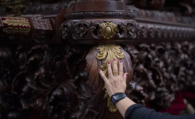 A worshipper prays placing her hand on the platform carrying a figure of Christ from the brotherhood of El Cerro, during Holy Week in Seville, Spain, Tuesday, April 15, 2025. (AP Photo/Emilio Morenatti)