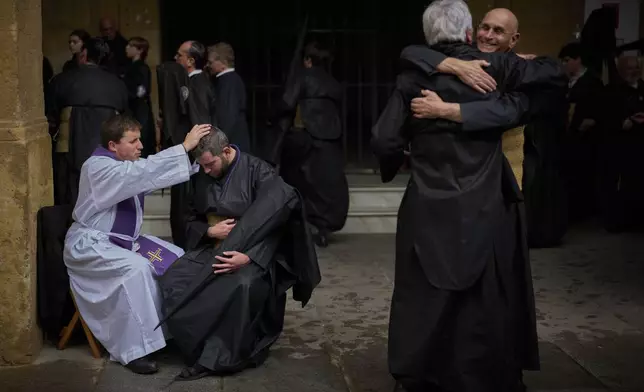 A penitent of the Los Estudiantes brotherhood is blessed after confessing to a priest as they prepare to go on procession during Holy Week in Seville, Spain, Tuesday, April 15, 2025. (AP Photo/Emilio Morenatti)