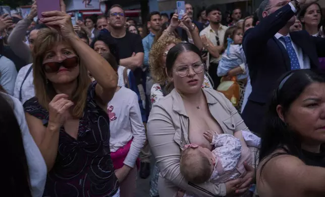 EDS NOTE: NUDITY - A woman breastfeeds as people look as the Christ of the brotherhood of La Estrella is carried out of the church to process through the streets of Seville, during Holy Week in Spain, Sunday, April 13, 2025. (AP Photo/Emilio Morenatti)