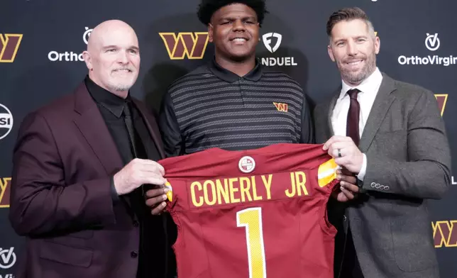 Washington Commanders first-round draft pick offensive tackle Josh Conerly Jr., center, holds his jersey with head coach Dan Quinn, left, and general manager Adam Peters, right, after an NFL football news conference in Ashburn, Va., Friday, April 25, 2025. (AP Photo/Luis M. Alvarez)