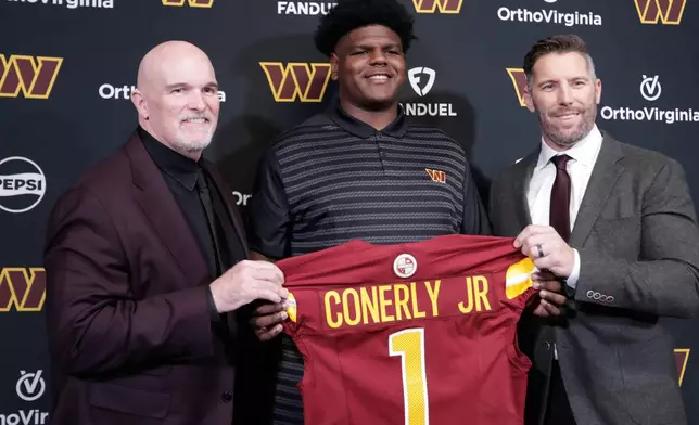 Washington Commanders first-round draft pick offensive tackle Josh Conerly Jr., center, holds his jersey with head coach Dan Quinn, left, and general manager Adam Peters, right, after an NFL football news conference in Ashburn, Va., Friday, April 25, 2025. (AP Photo/Luis M. Alvarez)