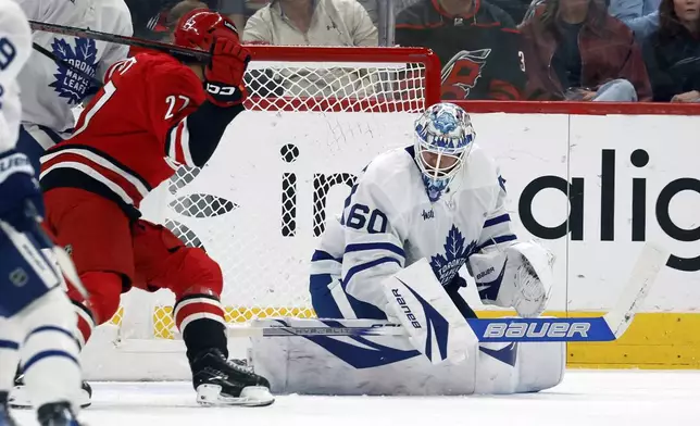Toronto Maple Leafs goaltender Joseph Woll (60) blocks a shot with Carolina Hurricanes' Tyson Jost (27) nearby during the first period of an NHL hockey game in Raleigh, N.C., Sunday, April 13, 2025. (AP Photo/Karl DeBlaker)