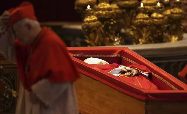 A cardinal walks past the body of Pope Francis, who will lie in state for three days, after it arrived in St. Peter's Basilica at the Vatican, Wednesday, April 23, 2025. (AP Photo/Francisco Seco)