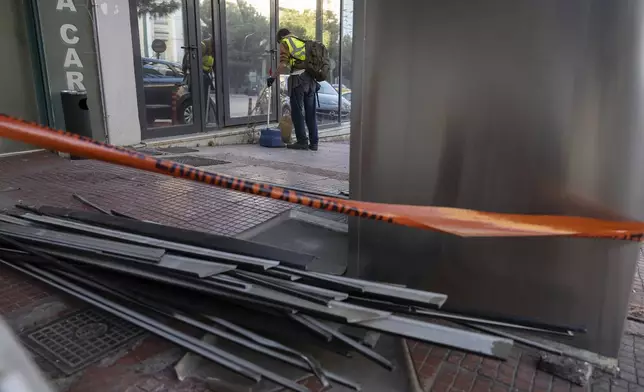 A municipal worker cleans the area outside Hellenic Train headquarters, Greece's main railway company, following a bomb explosion Friday night causing causing limited damage but no injuries, in Athens, Greece, on Saturday, April 12, 2025. (AP Photo/Yorgos Karahalis)
