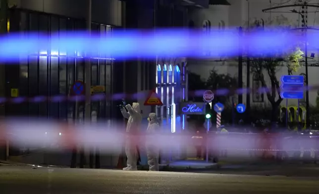 Police investigators wearing coveralls inspect the site after a bomb explosion outside of the Hellenic Train offices the company that runs Greece's railway, the first building on the left, in Athens, Greece, Friday, April 11, 2025. (AP Photo/Petros Giannakouris)