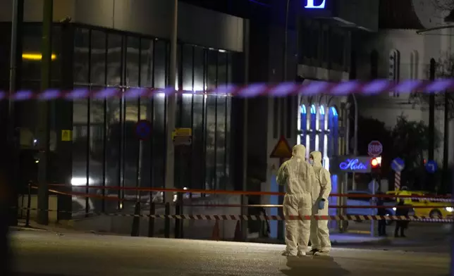 Police investigators wearing coveralls inspect the site after a bomb explosion outside of the Hellenic Train offices the company that runs Greece's railway, the building on the left, in Athens, Greece, Friday, April 11, 2025. (AP Photo/Petros Giannakouris)