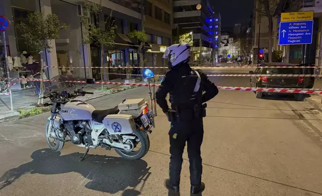 A policeman guards an area after a suspected bomb explosion outside of Hellenic Train offices the company that runs Greece's railway, the third building on the left, in Athens, Greece, Friday, April 11, 2025. (AP Photo/Derek Gatopoulos)