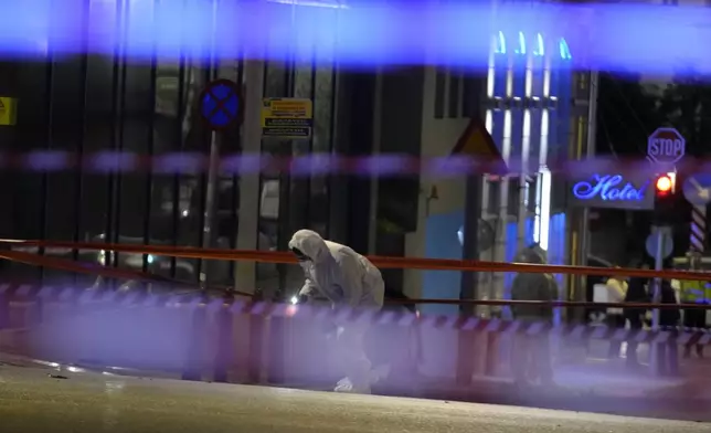 Police investigators wearing coveralls inspect the site after a bomb explosion outside of the Hellenic Train offices the company that runs Greece's railway, the first building on the left, in Athens, Greece, Friday, April 11, 2025. (AP Photo/Petros Giannakouris)